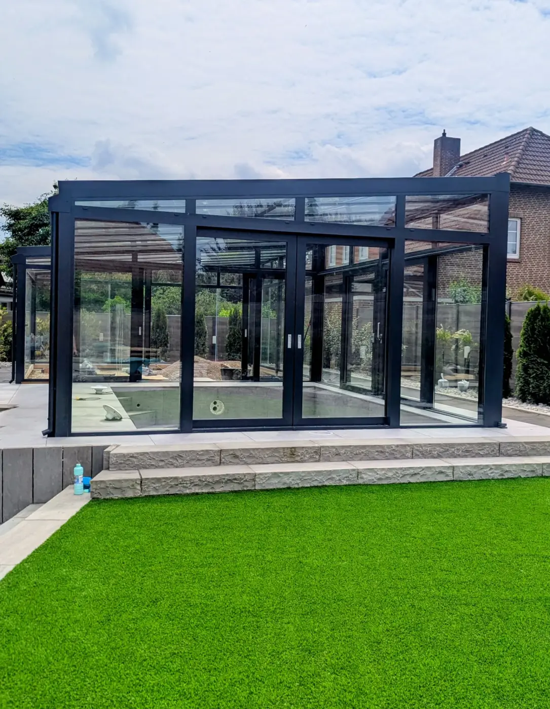 Fertig montierter Glas-Wintergarten mit anthrazitfarbenem Aluminiumrahmen über einer Poolterrasse in Hannover